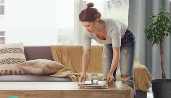 woman decluttering living room before carpet cleaning