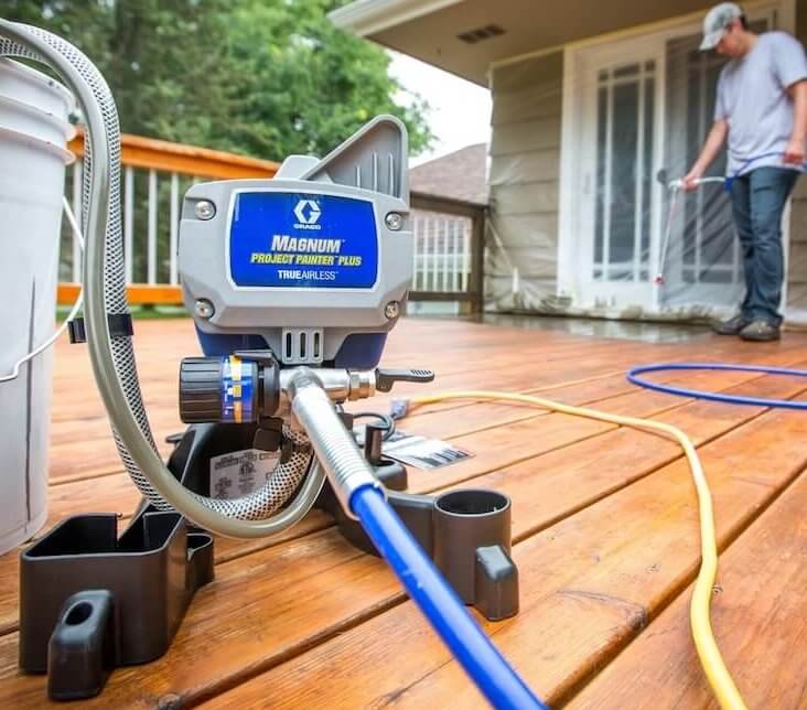 person using a Graco airless paint sprayer for sealing wood deck.